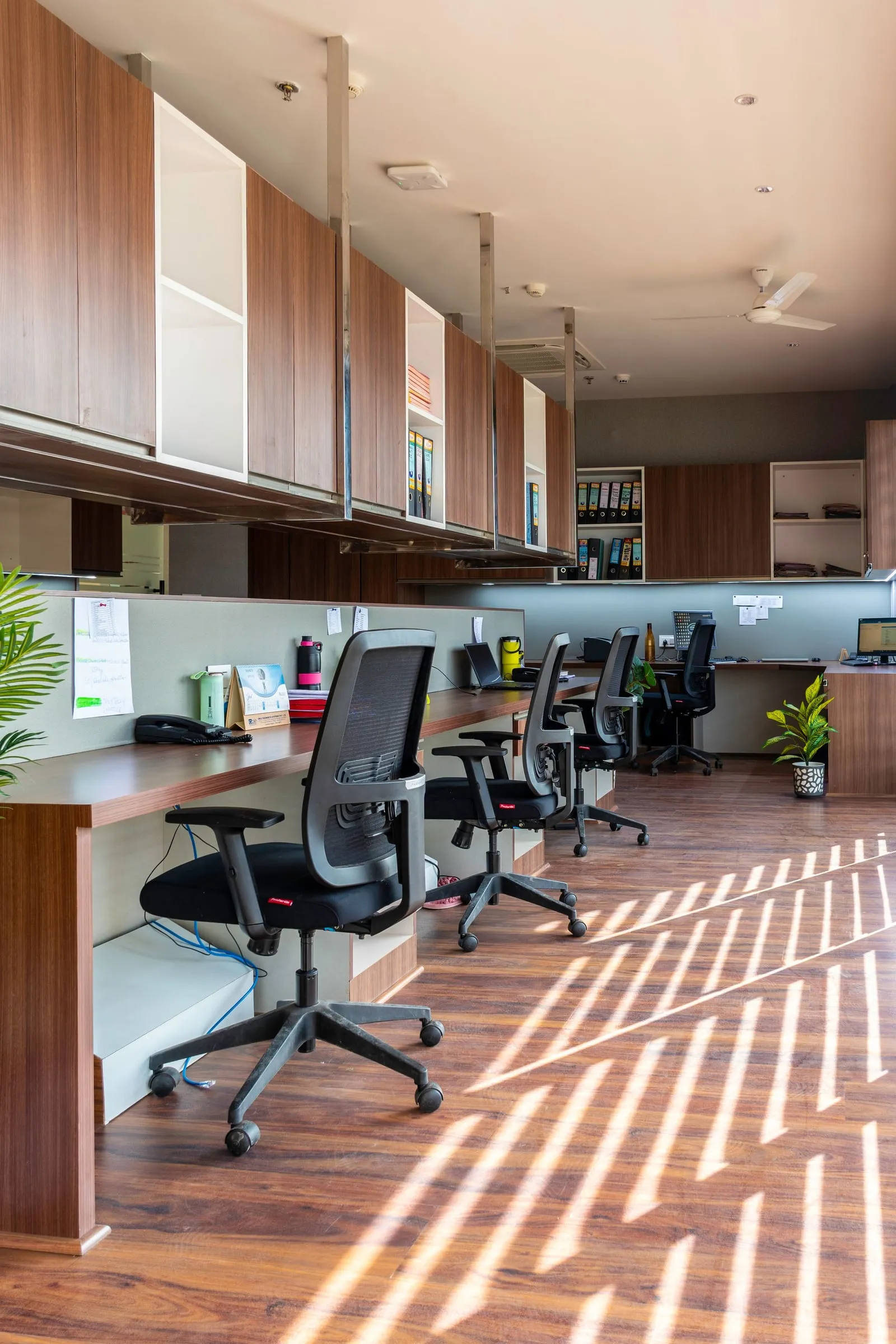 A commercial office with wood workstations, ergonomic chairs and overhead storage