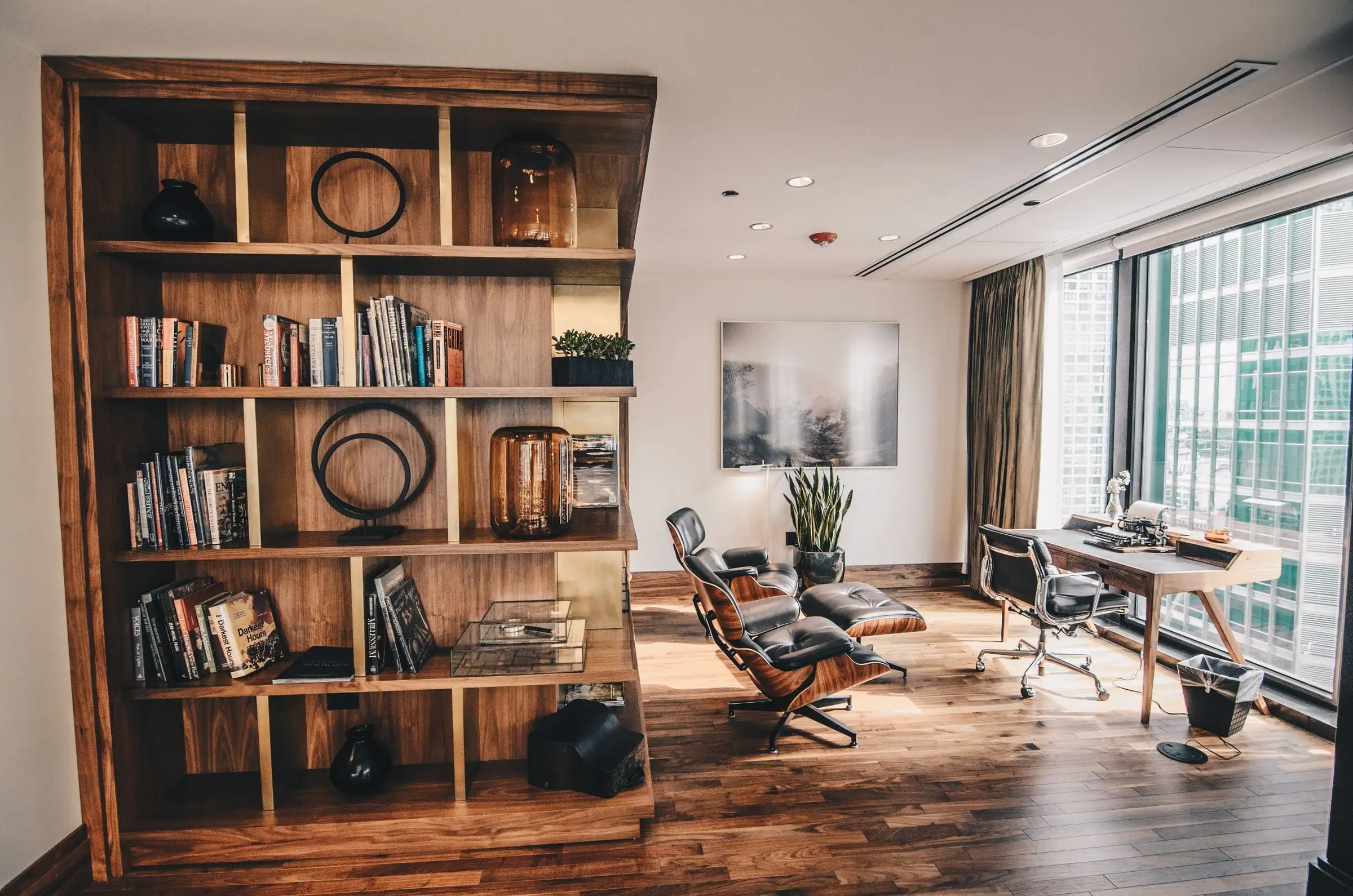 A residential home office with a built-in wooden bookshelf, lounge chair and desk