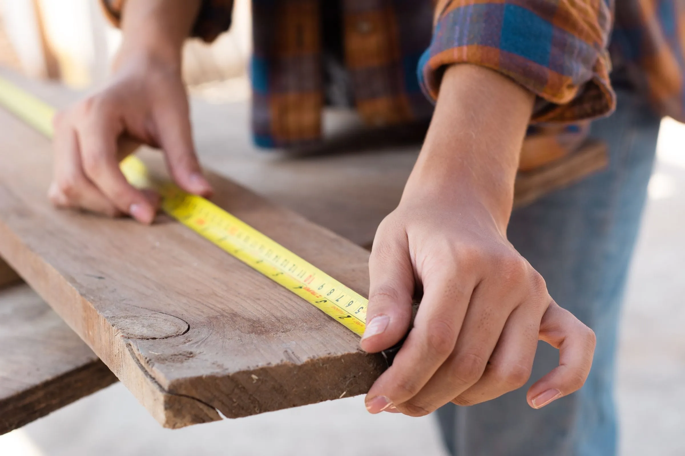 Hands measuring a wooden board with a tape measure